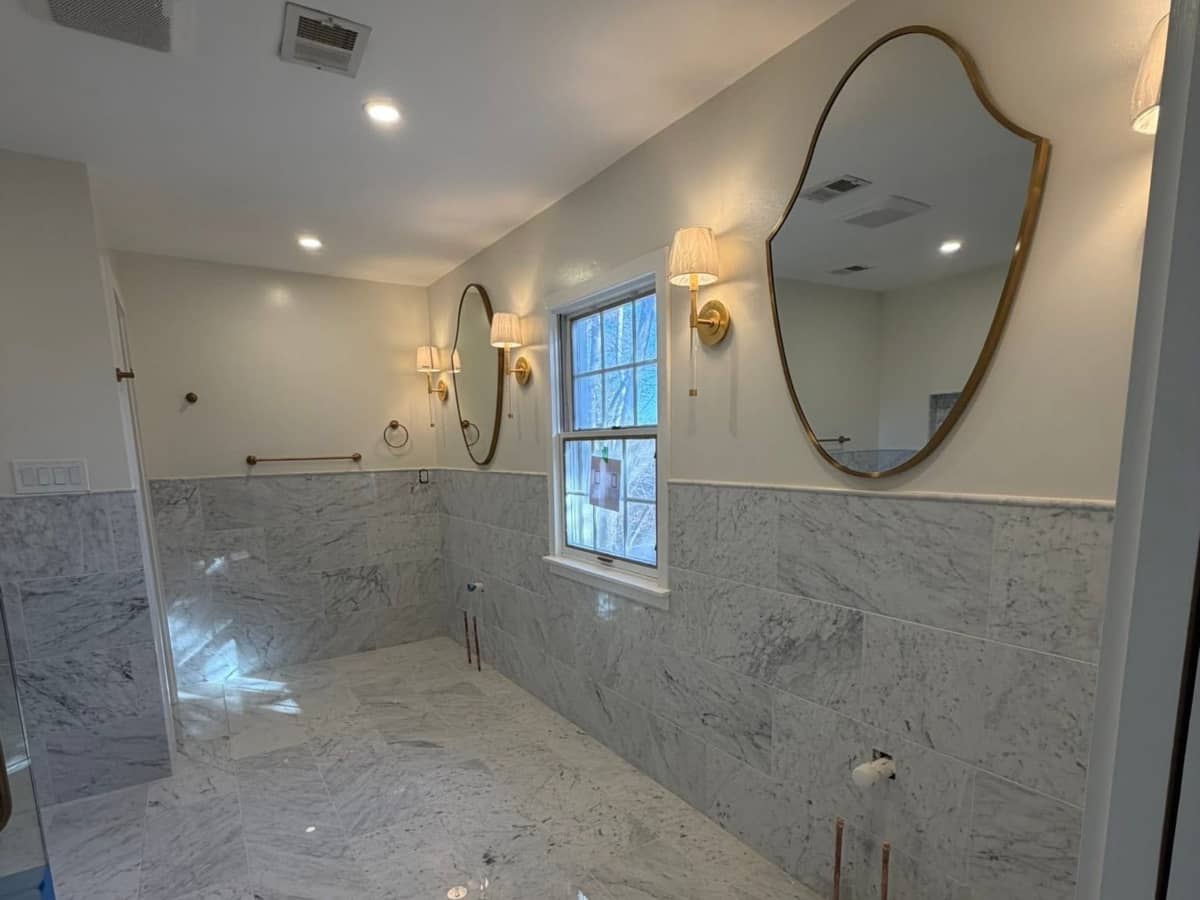 Bathroom remodel with marble tile walls and dual vanity mirrors