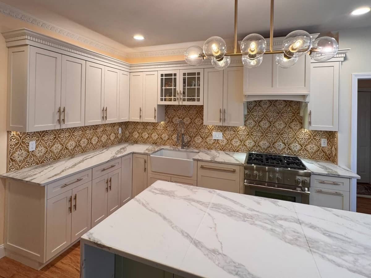 White kitchen remodel with patterned backsplash, marble island, and new lighting
