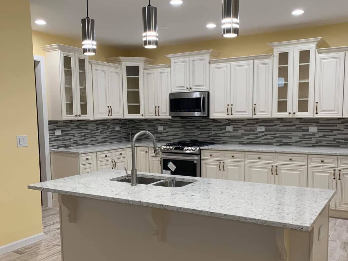 White kitchen remodel with granite island, tile backsplash, and stainless steel appliances